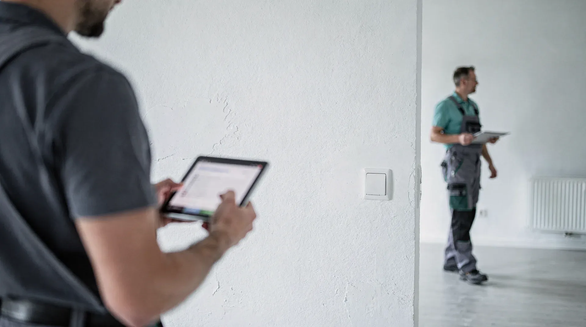 Person von hinten mit Tablet in einem leeren, hellen Raum bei einer Wohnungsabnahme