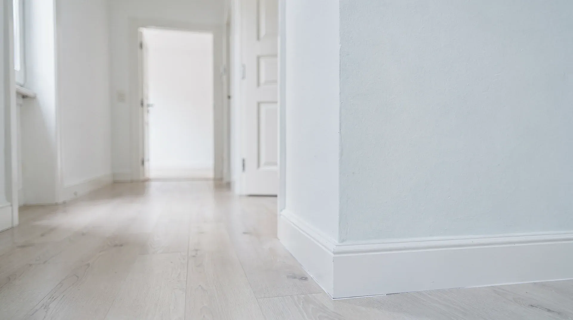 Heller leerer Wohnungsflur mit weißen Wänden und hellem Holzboden, ruhige Atmosphäre